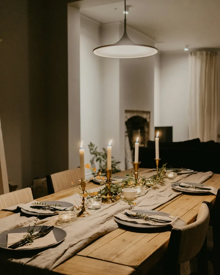 A dining table laid for guests in a home, candles lit and a fire behind